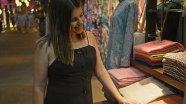 Gülümseyen genç bir kadın Dubai 'de geleneksel bir çarşıdan alışveriş yapar, tekstil ürünlerine dokunur ve kültürel deneyimden zevk alır..