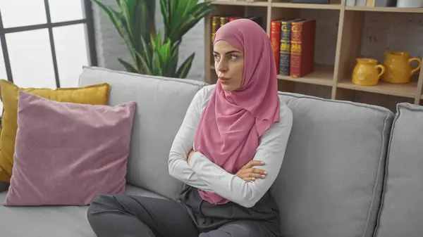 stock image A contemplative woman in a hijab sits with crossed arms in a cozy living room