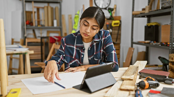 Молодая южно-азиатская женщина усердно работает в столярной мастерской, окруженная инструментами и деревом..