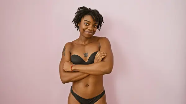 Stock image Confident young black woman with dreadlocks standing arms crossed against a pink wall in lingerie.