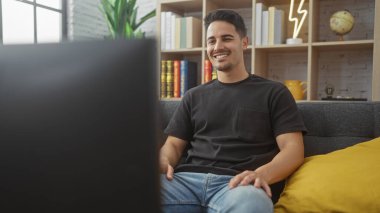 Modern bir oturma odasında dinlenirken sakallı genç bir İspanyol adam gülümsüyor..