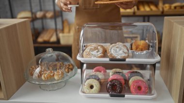 Fırında elinde kahve fincanı olan genç bir adam cam kapların altında çeşitli hamur işleri ve çörekleri sergiliyor.