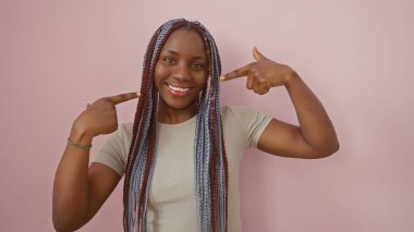 Gülümseyen ve örgülü bir kadın pembe bir arka plana karşı ağzını işaret eder.