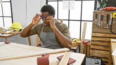 Odaklanmış bir adam, çeşitli aletlerle bir marangozluk atölyesinde koruyucu gözlük ayarlar..