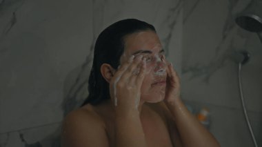 Genç bir İspanyol kadın modern bir evin banyosunda yüzünü sabunla yıkıyor..