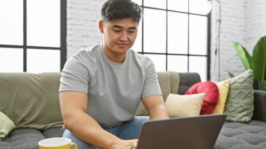 Modern bir apartman dairesinde dizüstü bilgisayar kullanan Çinli bir adam....