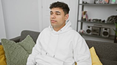 Kapüşonlu dalgın bir adam modern bir oturma odasında şık bir dekorla öylesine oturuyor..