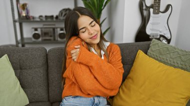 Memnuniyet duyan genç bir kadın evinde rahat bir anın tadını çıkarıyor, yarı kapalı gözler, gri bir kanepede kendini kucaklıyor.