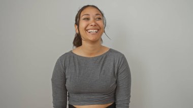 Çekici bir gülümsemesi olan neşeli, genç bir İspanyol kadın beyaz bir duvarın önünde duruyor, güzel ve pozitiflik saçıyor.