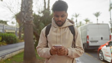 Afro-Amerikalı bir adam şehir arka planında akıllı telefondan mesaj atıyor..