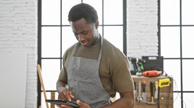 Afro-Amerikan adam marangozluk atölyesinde alet ve ekipmanla tablet kullanıyor.