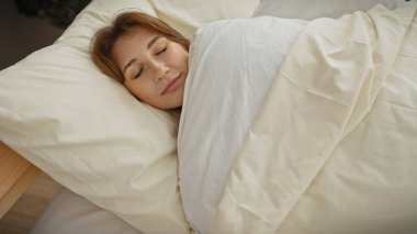 Beyaz bir yorganın altında, rahat, aydınlık bir yatak odasında huzur içinde uyuyan beyaz bir kadın..