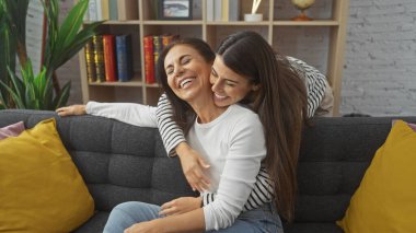 Keyifli bir anne-kız kanepede rahat bir oturma odasında kucaklaşıp aile sevgisini ve mutluluğunu simgeliyor.