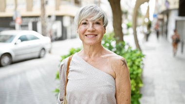 Gri saçlı, gülümseyen olgun bir kadın canlı bir şehir caddesinde güzellik ve kendine güven yayar..