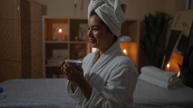 Güzel, genç, İspanyol bir esmer kadın kaplıcada dinlenen bir anın keyfini çıkarıyor. Kafasında beyaz bir bornoz ve havlu var. Huzurlu bir sağlık merkezinde elinde sıcak ışıklandırmalı bir fincan çay tutuyor..