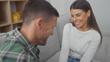 Gülümseyen İspanyol kadın evdeki kanepede bir erkekle sıcak bir anın tadını çıkarıyor. Aşk ve birliktelik temalarını çağrıştırıyor..