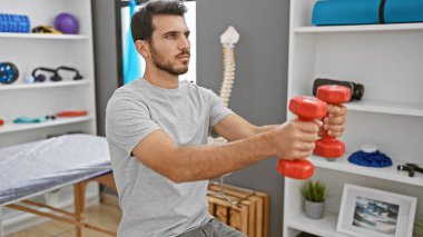 Bir rehabilitasyon kliniğinin terapi odasında dambıllarla egzersiz yapan odaklanmış bir İspanyol.