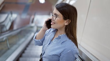Madrid metro istasyonunda yürüyen merdivende duran genç ve güzel İspanyol kadın telefonda konuşuyor.