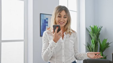 Modern ofis ortamında akıllı telefon kullanan gülümseyen beyaz iş kadını, bağlantı ve profesyonelliği iletiyor..