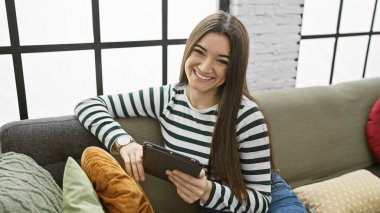 Tabletli gülümseyen genç İspanyol kadın kapalı bir koltukta oturuyor..