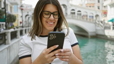 Qanat Quarter 'ın Doha, Katar' daki Venedik tarzı kanallarının yakınında akıllı telefon kullanan gülümseyen kadın..