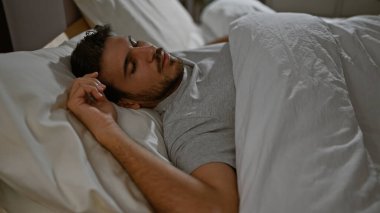Sakallı genç bir adam yatak odasında huzur içinde uyuyor, rahatlık ve rahatlık simgeliyor..