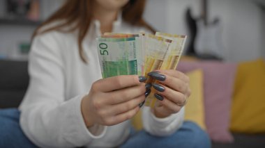 Kafkasyalı bir kadın Norveçli bir para birimini evde tutuyor, ev ortamında finansal tasarruf kavramını canlandırıyor..