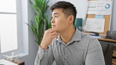 Düşünceli Asyalı bir adam modern bir ofis ortamında, profesyonelliği ve düşünceliliği somutlaştırıyor..