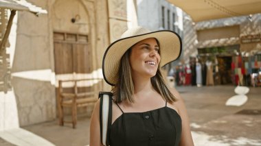 A smiling woman in a hat explores a traditional souq market in dubai under a sunny sky. clipart