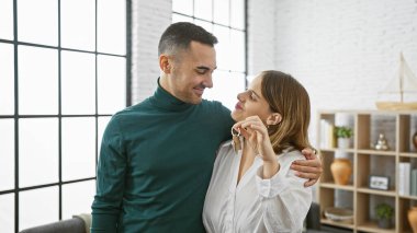 Kadın ve erkek modern bir salonda kucaklaşıyorlar, ellerinde anahtarlar, yeni evi sembolize ediyorlar..