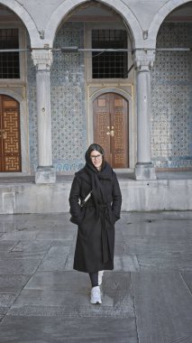 Siyahlar içinde gülümseyen genç bir kadın İstanbul 'daki antik bir divanın önünde duruyor..