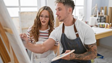 Yaratıcı bir erkek ve kadın, parlak bir stüdyoda ressamlık yaparak, tuvalde birlikte resim yaparlar..