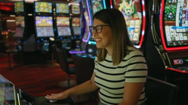 Neşeli bir kumarhanede kumar makinesinde oynayan gülümseyen genç bir kadın..