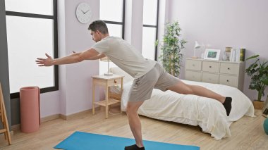 Genç adam yoga minderi ve minimalist dekoruyla modern bir yatak odasında geriniyor..