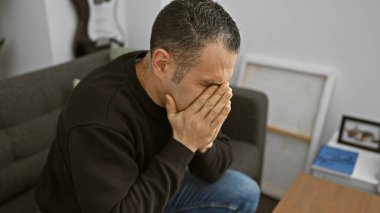 Sıkıntılı bir İspanyol adam, elleri kapalı evde oturuyor, yüzünü kapatıyor, evde hüzün tasvir ediyor..