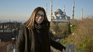 Güneşli bir İstanbul gününde Sultan Ahmet Camii 'nin önünde gözlüklü, gülümseyen kadın.