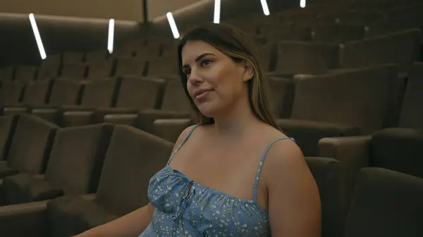 stock image A young adult hispanic brunette woman sits contemplatively in a cinema hall's empty seats.