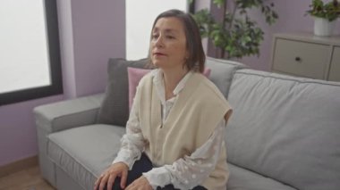 Modern bir oturma odasında oturan orta yaşlı bir kadın sırt ağrısı çekiyor.