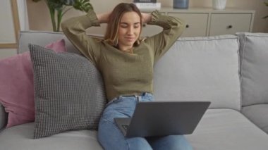 Güzel, sarışın bir kadın modern bir koltukta elleri başının arkasında, dizüstü bilgisayarı yanında, rahat bir şehir merkezinde dinleniyor..