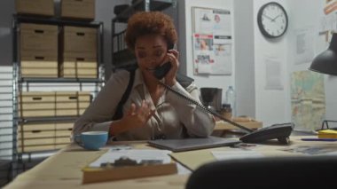 Belgelerle ve telefonla konuşarak polis karakolunda çalışan Afrikalı Amerikalı kadın dedektif..