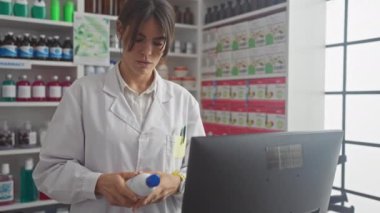 Odaklanmış bir kadın eczacı, bir eczanede bilgisayar üzerinde çalışırken ürünü analiz eder.