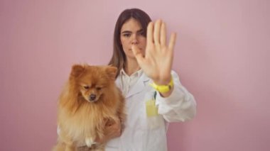 Ciddi bir ifadeyle savunmada duran kendine güvenen genç İspanyol kadın, pembe bir arka planda izole edilmiş bir el hareketi yapıyor.