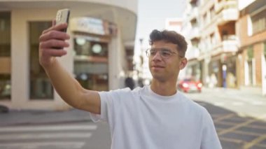 Genç İspanyol bir adam gün boyunca şehir merkezinde bir caddede selfie çekiyor.