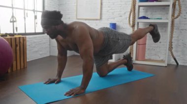 Genç, Afrikalı Amerikalı bir adam spor salonunda egzersiz yapıyor. Spor şortu ve saç bandı giyiyor. Forma ve dayanıklılık eğitimine odaklanıyor..