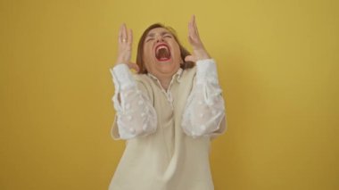 Orta yaşlı İspanyol kadın, izole edilmiş sarı arka planda duruyor, onun hayal kırıklığını ifade ediyor; onun çılgın, çılgın ve agresif bağırma, bağırma ve bağırma ifade ile kollarını birleştiriyor
