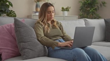 Genç, sarışın, beyaz bir kadın şehir merkezindeki bir kanepede dizüstü bilgisayar kullanırken hayal kırıklığını ifade ediyor..