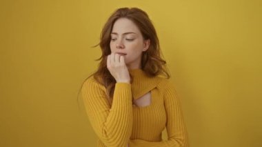 Süveter giyen genç beyaz kadın gergin ve gergin görünüyor. Ağzı tırnak yiyen eller. Anksiyete izole edilmiş sarı arkaplan