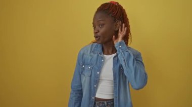 Afrika kökenli Amerikalı bir kadın, izole edilmiş sarı arka planda duruyor, kot gömlek giyiyor, kulağının üstünde eli ile bir söylenti dinliyor, sağırlık ve dedikodu kavramını gözler önüne seriyor.