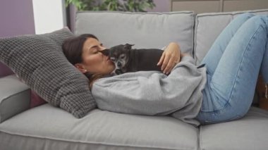 Genç bir kadın sıcak bir oturma odasında kanepede dinlenirken Chihuahua 'sını sevgiyle öper..