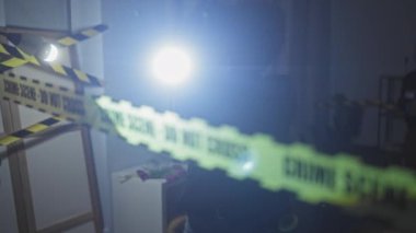 El fenerli siluetli dedektifler uyarı bandıyla işaretlenmiş bulanık oturma odasının içindeki suç mahallini araştırıyorlar..